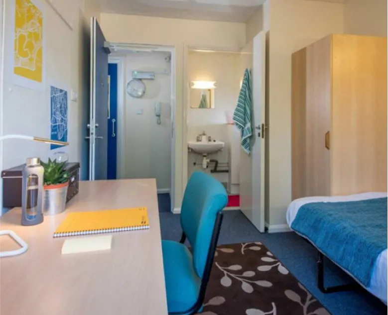 A tidy student bedroom with a made bed, desk and study lamp